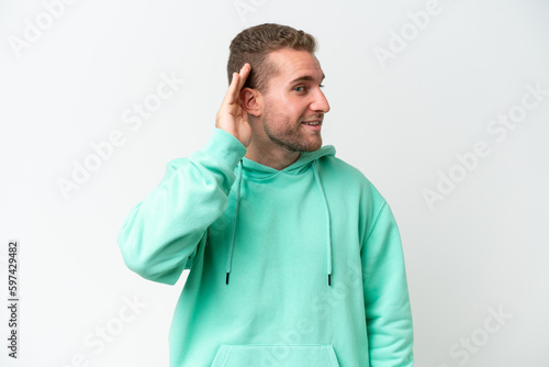 Young handsome caucasian man isolated on white background listening to something by putting hand on the ear © luismolinero