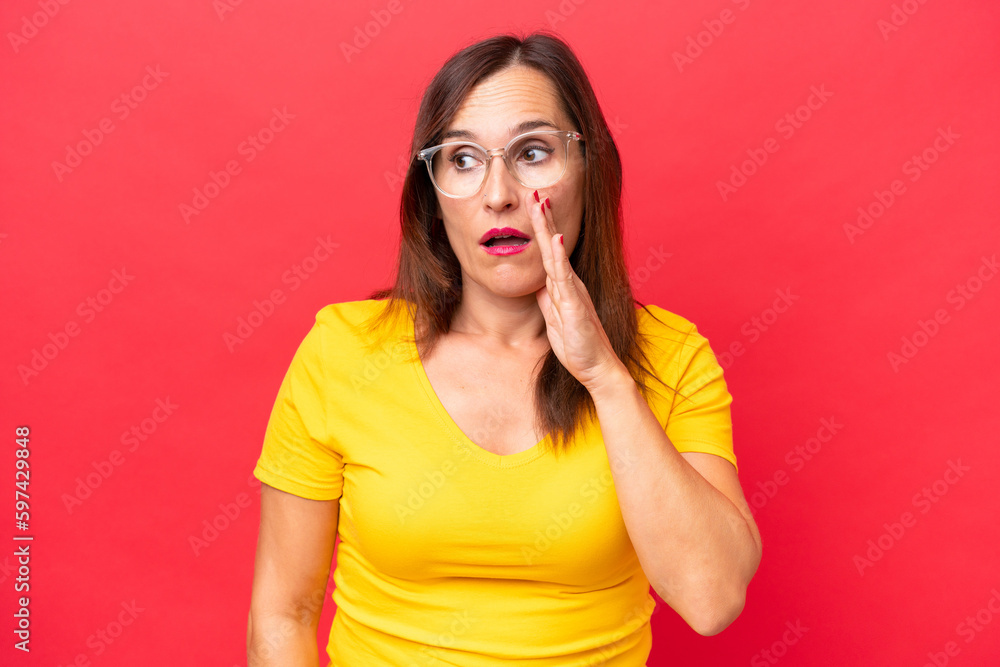 Middle-aged caucasian woman isolated on red background whispering something with surprise gesture while looking to the side Middle-aged caucasian woman isolated on red background whispering something with surprise gesture while looking to the side