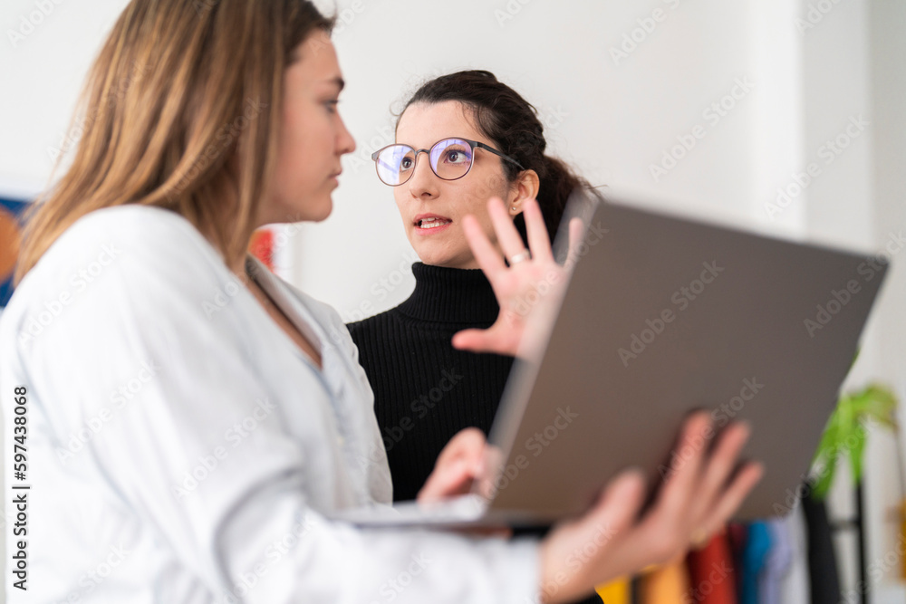 Positive young female team in casual clothes and checking laptop while working on project in creative workspace together Positive young female team in casual clothes and checking laptop while working on project in creative workspace together