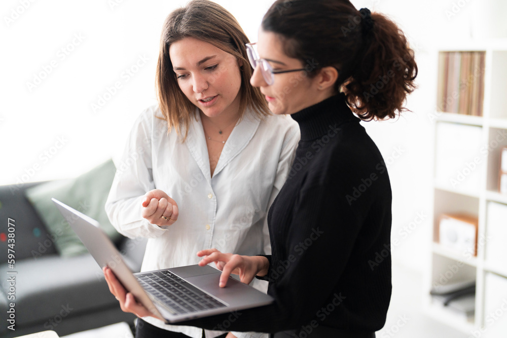 Positive young female team in casual clothes and checking laptop while working on project in creative workspace together Positive young female team in casual clothes and checking laptop while working on project in creative workspace together