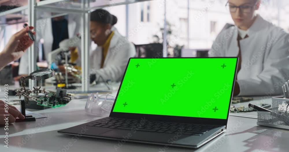 Laptop Computer with Green Screen Mock Up Display Standing on a Table in a Science Class Laboratory. Diverse Students Practicing Soldering Electronic Components for Their Tech Projects Laptop Computer with Green Screen Mock Up Display Standing on a Table in a Science Class Laboratory. Diverse Students Practicing Soldering Electronic Components for Their Tech Projects