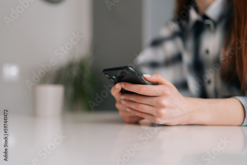 Closeup cropped shot of unrecognizable young woman texting message on mobile phone for communication and chatting on social online sitting at white desk. Closeup hands of lady typing using smartphone.