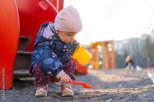 The child is using a children's shovel while playing with sand on the playground. A little girl playing at the playground outdoors. Outdoor creative activities for kids.