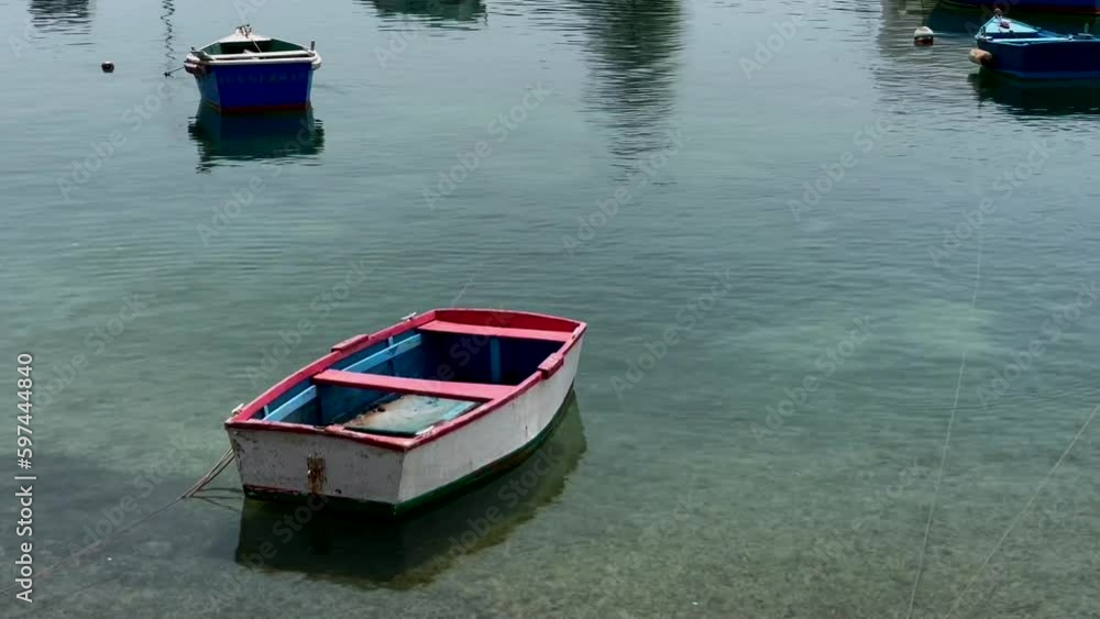 This video shows a small boat floating on a serene lake in a quaint village. The water is calm and reflects the surrounding greenery. The boat moves slowly and peacefully
