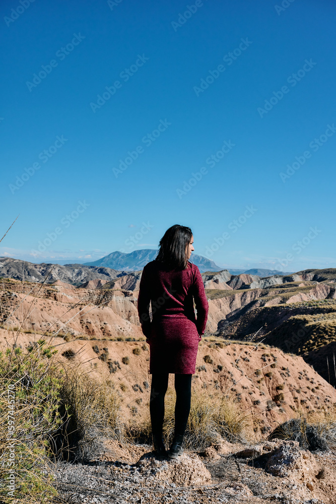 A young woman with her back turned in front of the entrance to a desert in broad daylight.