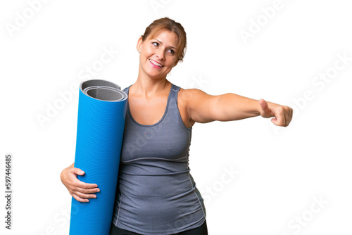 Middle-aged sport woman going to yoga classes while holding a mat over isolated background giving a thumbs up gesture