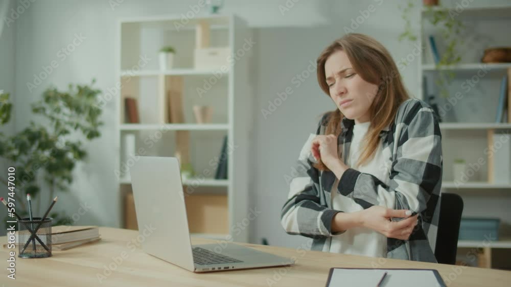 Focused Woman Work at a Table With a Laptop Suddenly Feeling Pain at Elbow. Woman Feeling Tired of Long Sedentary Lifestyle. Try to Relax and Relieve Pain by Massages Her Hand. Office Syndrome. Focused Woman Work at a Table With a Laptop Suddenly Feeling Pain at Elbow. Woman Feeling Tired of Long Sedentary Lifestyle. Try to Relax and Relieve Pain by Massages Her Hand. Office Syndrome.