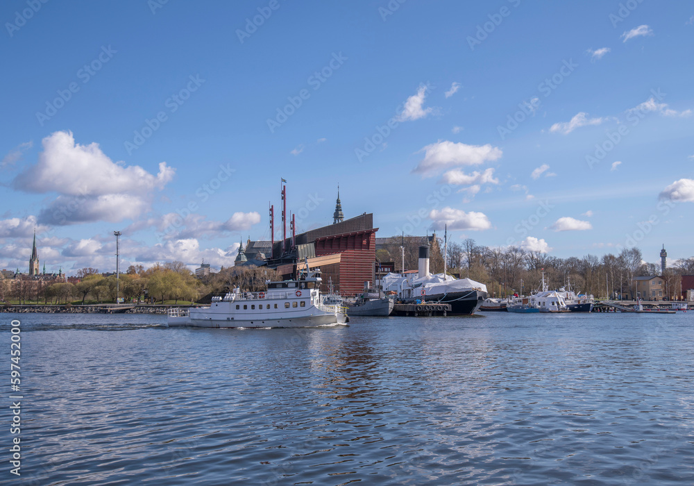 Harbor commuting ferry passing the maritime museum boats and the Vasa museum, a sunny spring day with cumulus clouds in Stockholm