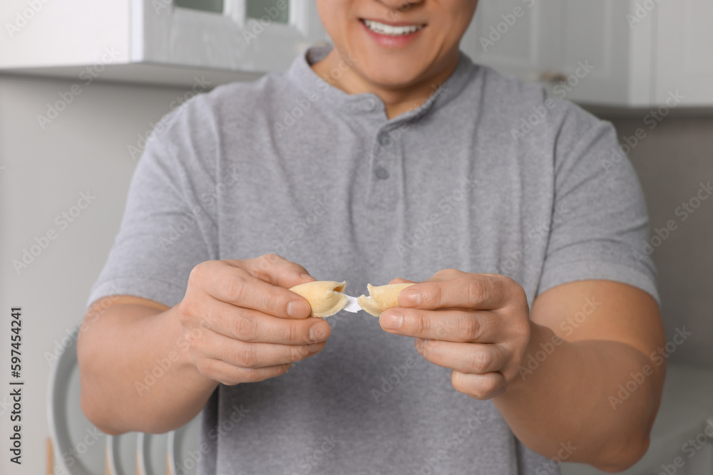 Happy man holding tasty fortune cookie with prediction indoors, closeup Happy man holding tasty fortune cookie with prediction indoors, closeup