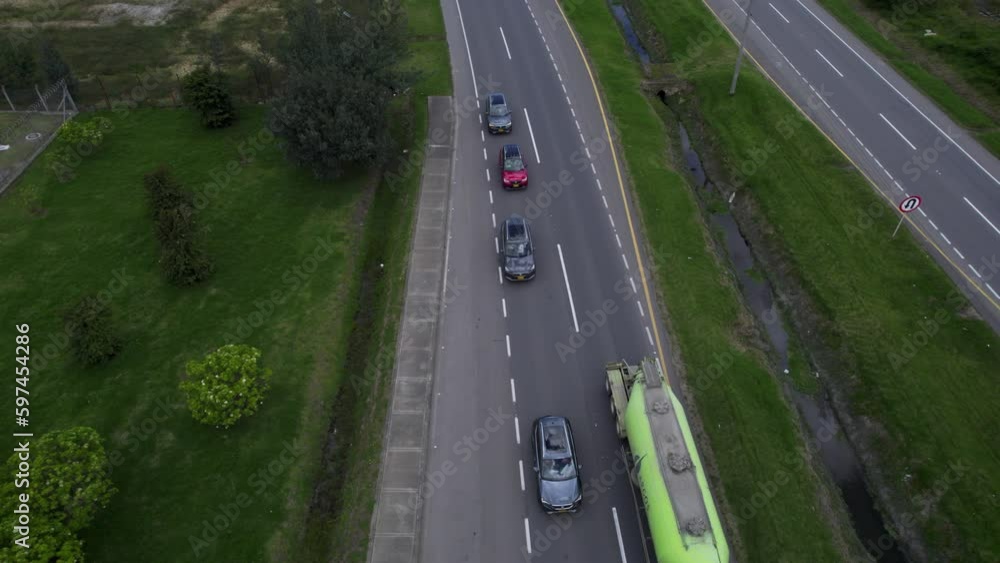 Overhead drone clip over lorry overtaking a queue of cars, moving along a two lane road lines with grass and bushes Overhead drone clip over lorry overtaking a queue of cars, moving along a two lane road lines with grass and bushes