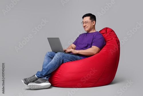 Happy man with laptop sitting in beanbag chair against grey background