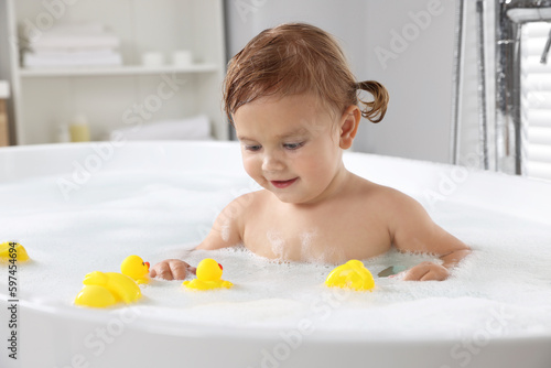 Cute little girl with rubber ducks in foamy bath at home