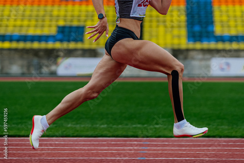close-up female runner sprinter running track stadium, summer athletics championships, kinesiotaping on lower leg