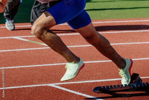 close-up legs male runner running in starting blocks sprint race, summer athletics championships