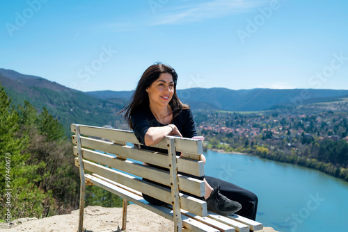 Traveler woman sitting on a bench high above a blue lake with stunning view . 
