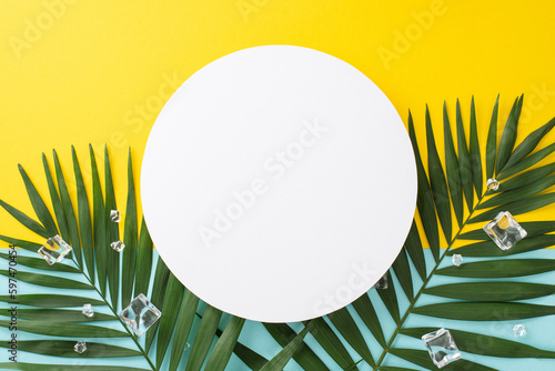 Chill out and enjoy the summer vibe with a top view flat lay of green palm leaves and ice cubes on blue and yellow background. Ideal for vacation concept with empty circle for text or branding