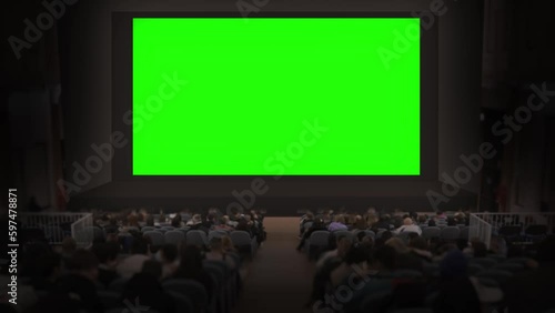 People sitting in theater chairs watching big green screen