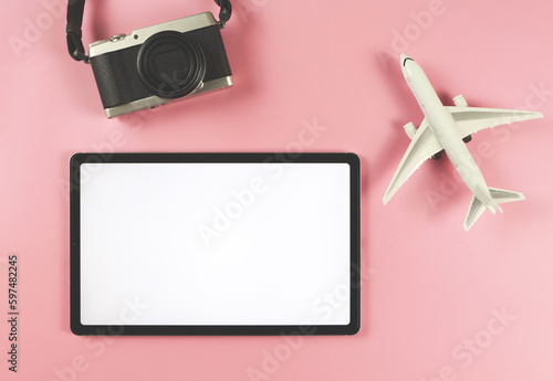 flat lay of digital tablet with blank white screen, airplane model and digital camera isolated on pink background. travel planning concept.