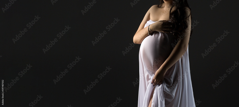 A pregnant woman in a white dress on a black background. Studio pregnancy photo shoot. Space for text. Beautiful pregnancy. A pregnant woman in a white dress on a black background. Studio pregnancy photo shoot. Space for text. Beautiful pregnancy.