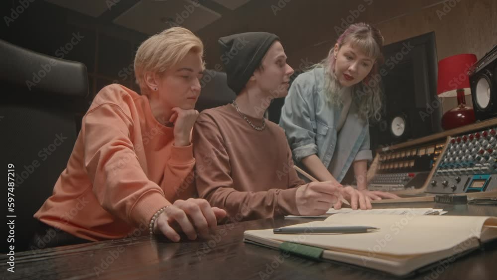 Group of three young Caucasian musicians coworking on lyrics of new song in recording studio Group of three young Caucasian musicians coworking on lyrics of new song in recording studio