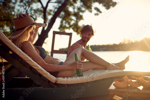 A young couple in swimsuit sitting on sunbeds and enjoying the sun and drink on the river bank. Summer, river, vacation © luckybusiness