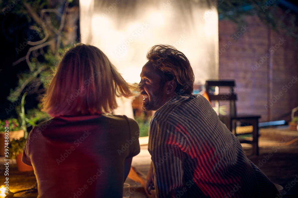 A young couple enjoying a night cinema in the bar at the river bank. Night, summer, bar, river