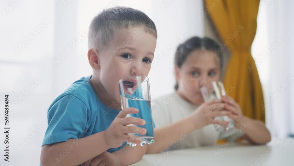 Children indoors drinking glassware water. Crisis clean a drinking water. children in kitchen drink clean water. baby boy drinking water from a glass close-up. Little children lifestyle drink Children indoors drinking glassware water. Crisis clean a drinking water. children in kitchen drink clean water. baby boy drinking water from a glass close-up. Little children lifestyle drink