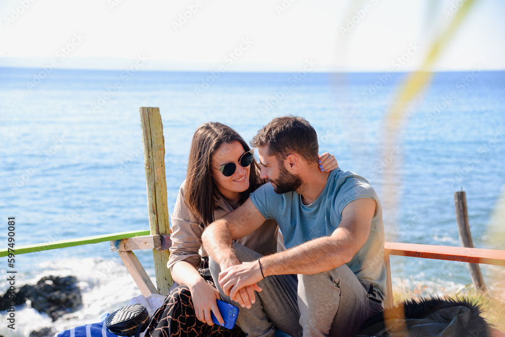 Cute couple on a vacation. Sitting on the beach looking to each other and smiling. Beautiful summer view.