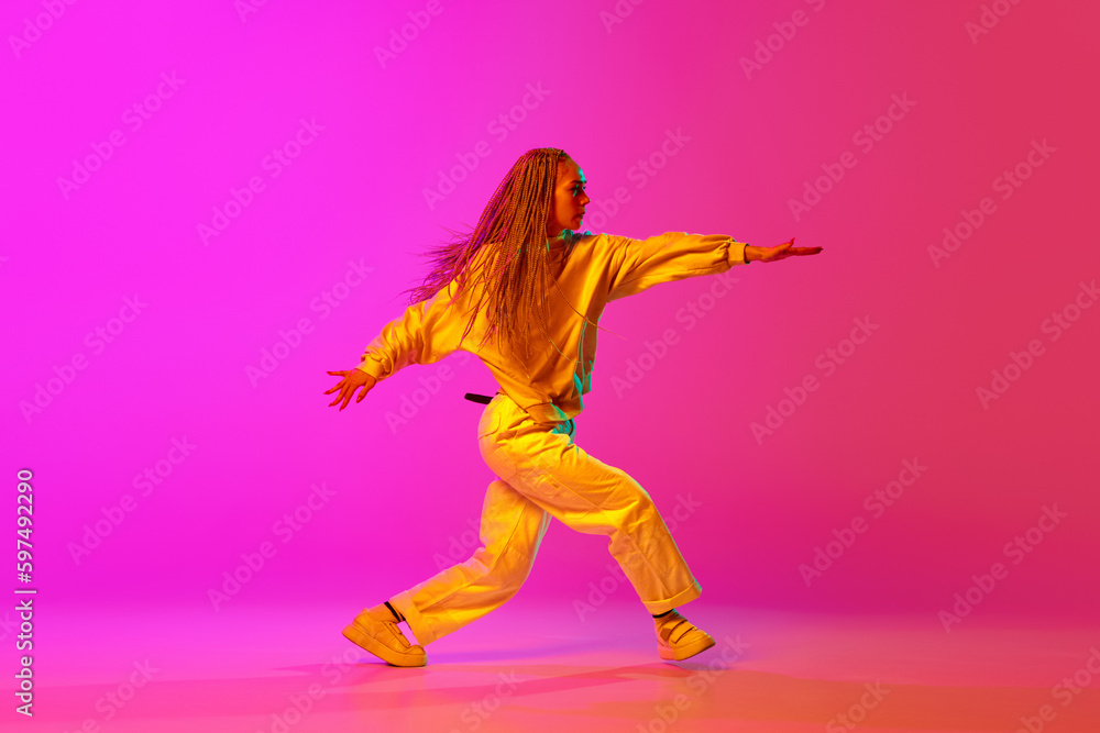 Portrait with one young attractive woman, dancer with pigtails dancing over gradient pink background in neon light. Side view. Contemporary dance style