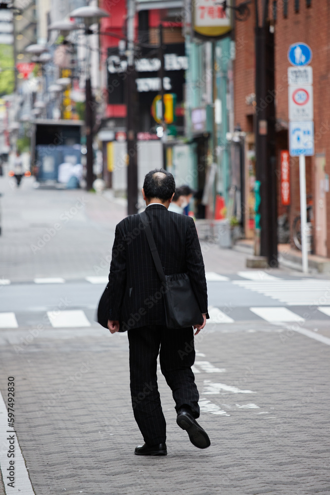 朝の繁華街を歩く一人の中年サラリーマンの後ろ姿