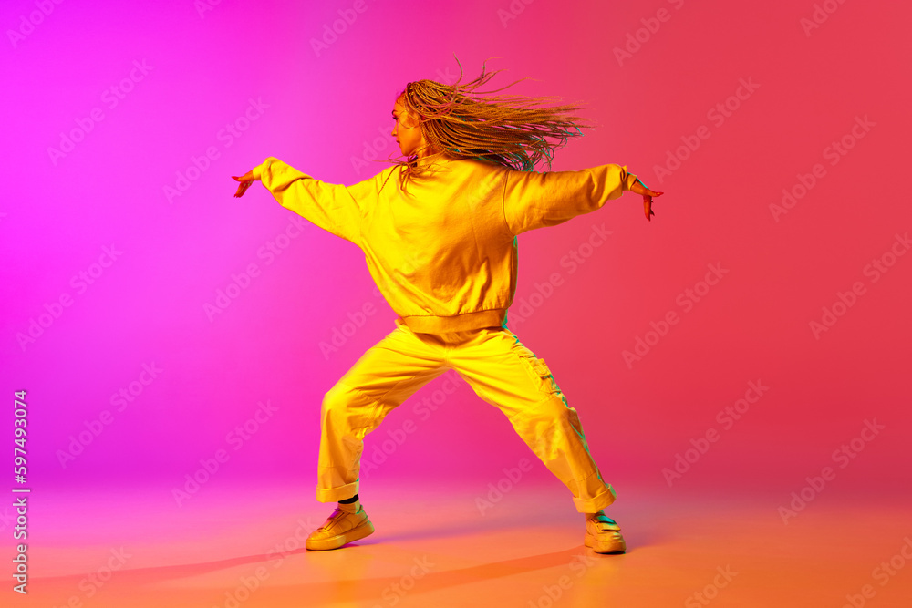 Portrait with one charming girl, dancer with dreadlocks dancing over gradient pink background in neon light. Contemporary dance style