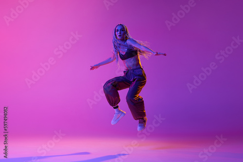 One dancer, woman wearing casual clothes jumping up in motion over gradient purple neon background. Levitate