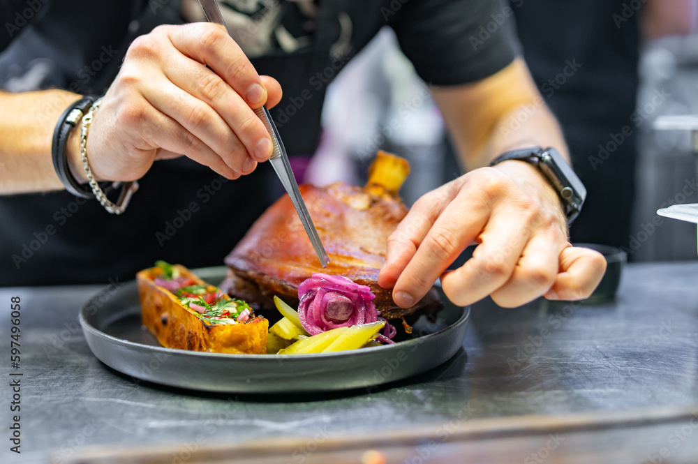 chef hand cooking Baked Pork knuckle with vegetables on plate in kitchen
