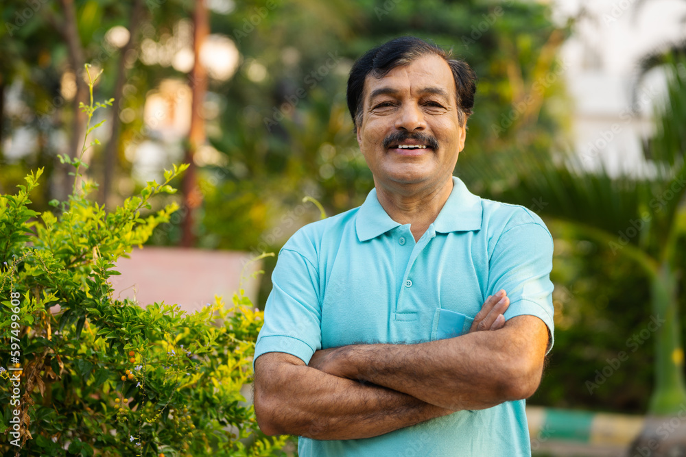 Happy smiling indian senior man standing with crossed arms by looking camera at park - concept of successful, confident and satisfied Happy smiling indian senior man standing with crossed arms by looking camera at park - concept of successful, confident and satisfied