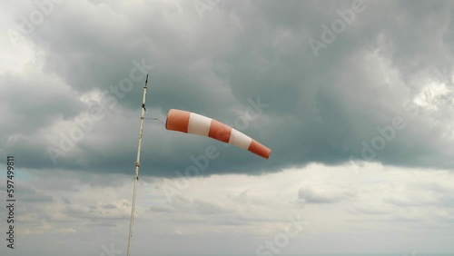 Against the cloudy sky, a white and red windsock dangles in the wind. Mounted on a pipe with peeling paint. It's a cloudy, windy day