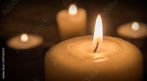Large lit candle in the foreground and other smaller candles in the blurred background
