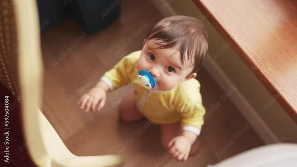baby with a pacifier close-up trying to get up liens on a chair. family baby child dream concept. baby at home looking at camera indoors lifestyle