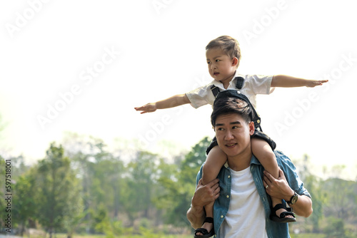 Young Asian father carry boy on shoulder having fun outdoors activity together