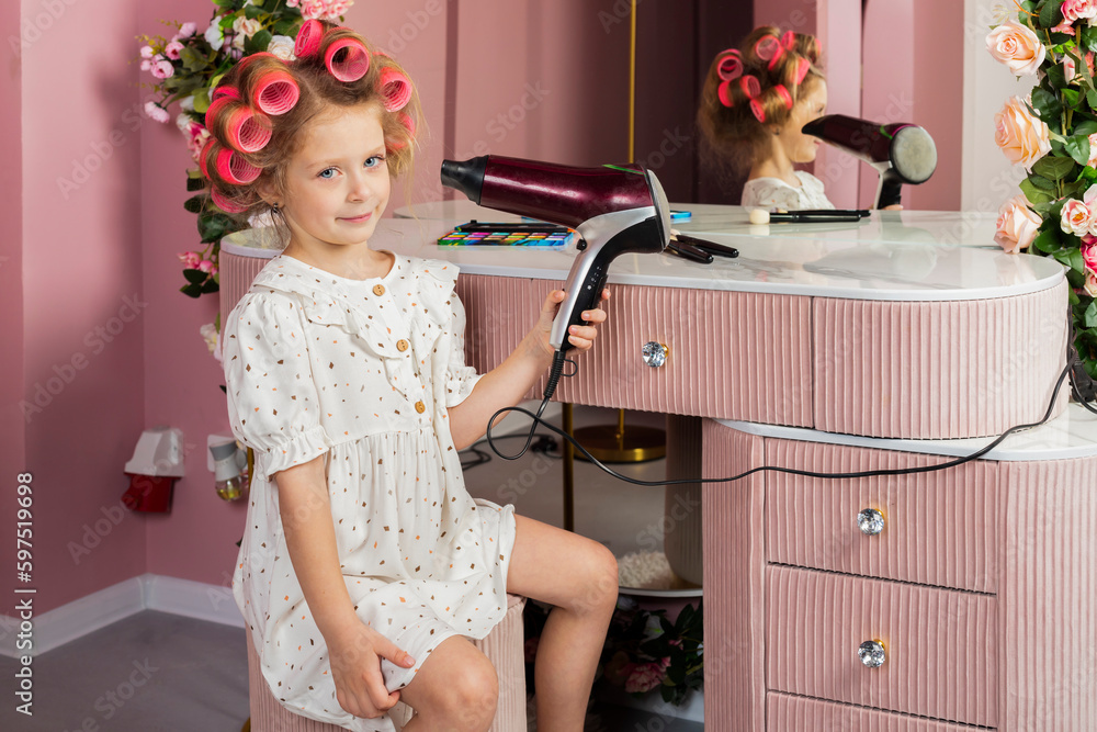Little girl wearing hair rollers and white polka dot dress sits in the ...