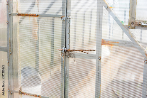 The greenhouse door is closed with a branch. Greenhouse made of plastic panels.
