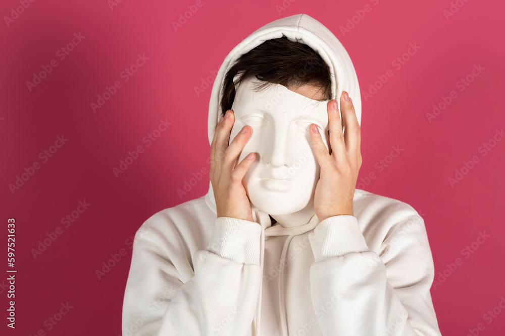 Portrait of a Suspicious young man in white hoodie covering face with a mask. Secret admirer, Hidden identity concept. Isolated on pink background. Portrait of a Suspicious young man in white hoodie covering face with a mask. Secret admirer, Hidden identity concept. Isolated on pink background.