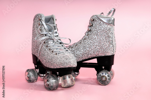 Pair of glitter silver stylish roller skates on pink background. photo