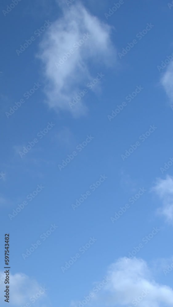 A time-lapse recording of a clear blue sky with white, cottony clouds moving across. Vertical video. A time-lapse recording of a clear blue sky with white, cottony clouds moving across. Vertical video.