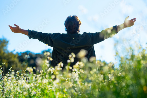 Back view of man outstretching arms in a green field. Travel destination tourism. Outdoor leisure activity and happiness concept lifestyle. Life balance. Success and mindful positive attitude. People photo