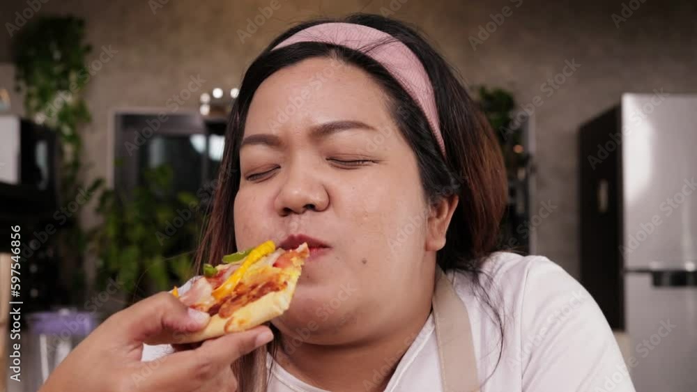 Happy asian fat woman eating pizza with relish in the kitchen at home. Fast food concept. lose weight Happy asian fat woman eating pizza with relish in the kitchen at home. Fast food concept. lose weight
