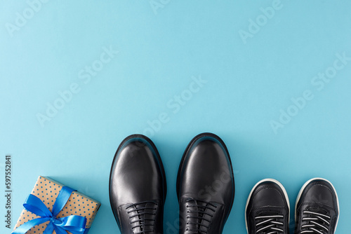 Father's Day celebration concept. Top view flat lay of gift box with ribbon stylish shoes father and child on light blue background with empty space for greeting text or message