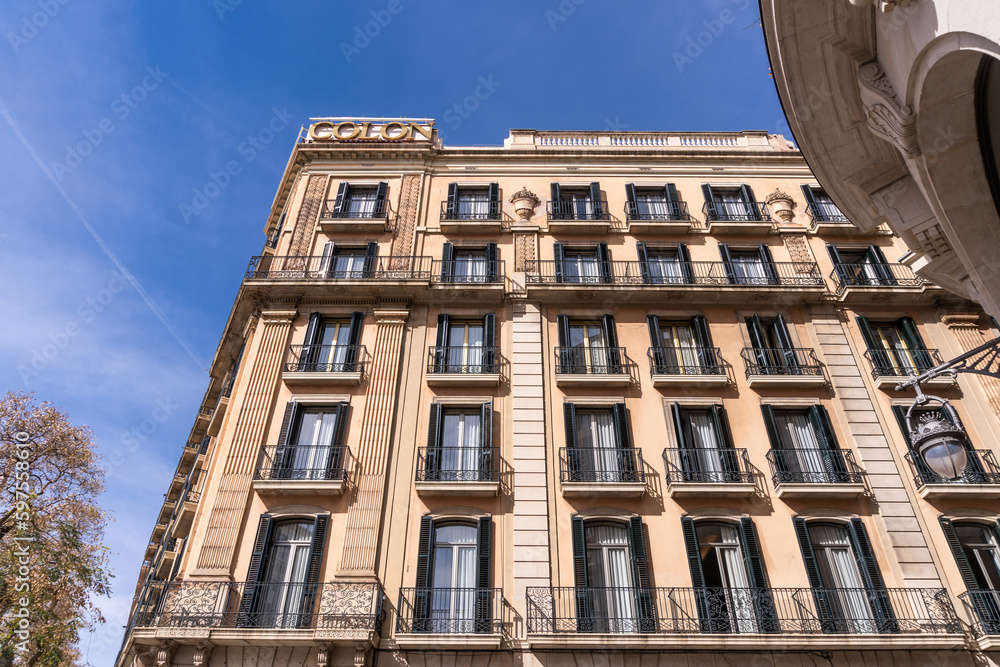 A majestic Barcelona tower block, adorned with intricate Art Nouveau architecture and windows. It stands majestically against the backdrop of a cloudy sky in its residential neighborhood.
