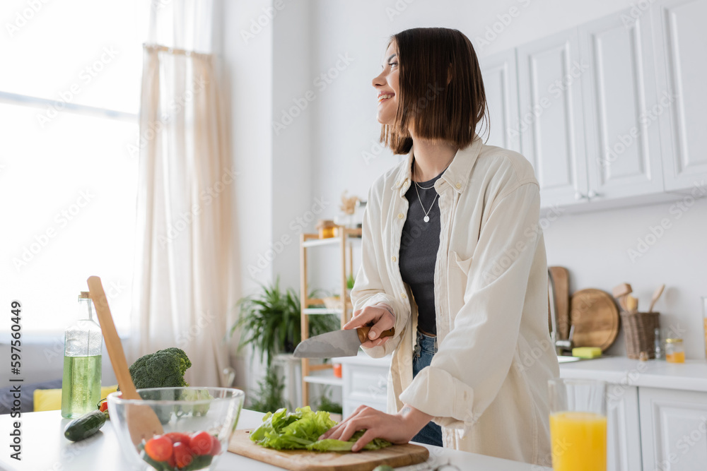 Smiling young woman cutting lettuce near orange juice and salad in kitchen. Smiling young woman cutting lettuce near orange juice and salad in kitchen.