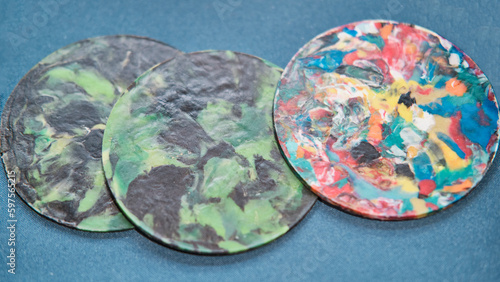 Colorful three trivets or coasters made of multicolored recycled plastic lids
