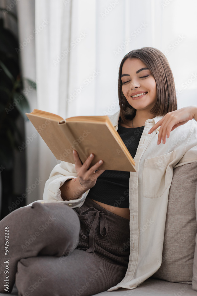 Positive woman reading book while resting on couch at home. Positive woman reading book while resting on couch at home.